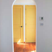 color garden 26 が手掛けた横浜個人邸・廊下への出入り口。白い壁にアーチが作られ、廊下側には黄色いドアが2つ並んでいる。床は明るい色調のフローリング。